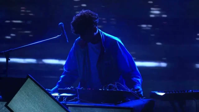 cash performing at an electronic instrument on a blue-lit stage.