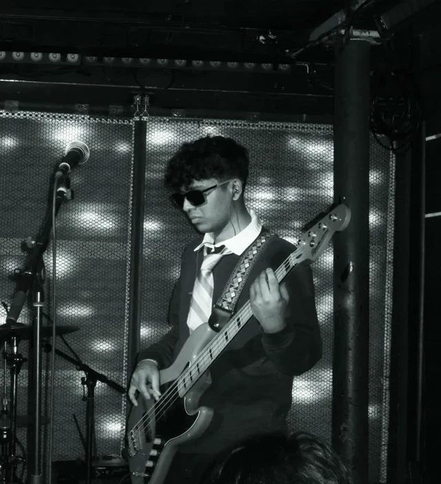 Bass guitarist performing beside a microphone, photographed in black and white.