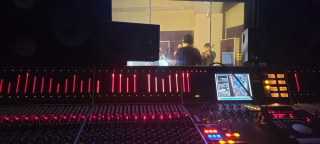 Mixing console with red faders and a monitor in a dark control room.